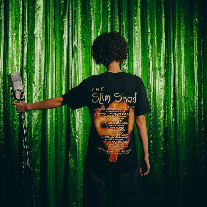 Back view of the Eminem SSLP25 Fire T-shirt worn by a model holding a microphone, highlighting the shirt’s back print with song lyrics and a flaming microphone.
