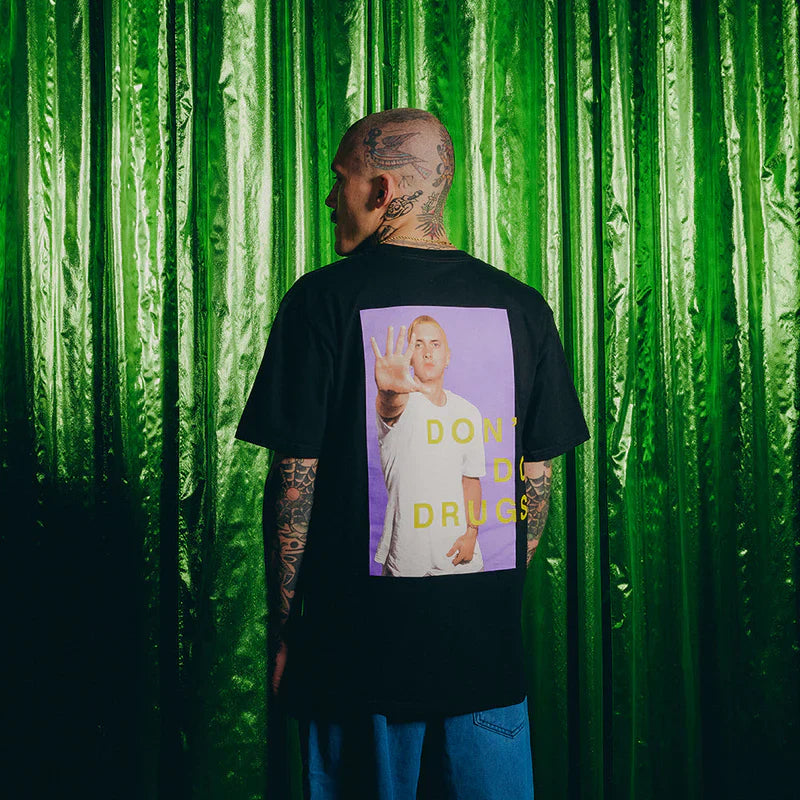 Close-up of the back of Eminem's SSLP25 PSA black T-shirt, with a prominent 'Don't Do Drugs' slogan over a purple background and Eminem holding up a peace sign.