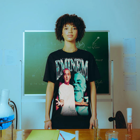 Model wearing the Eminem SSLP25 Chrome T-shirt in a classroom setting, displaying a vibrant print of Eminem's early persona with chrome-style lettering.