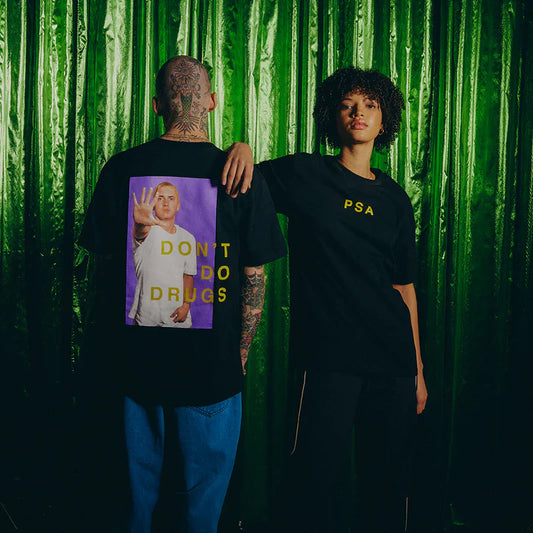 Male and female models showcasing the front and back of the Eminem SSLP25 PSA T-shirt in black with a bold 'Don't Do Drugs' message and Eminem's photo on the back.